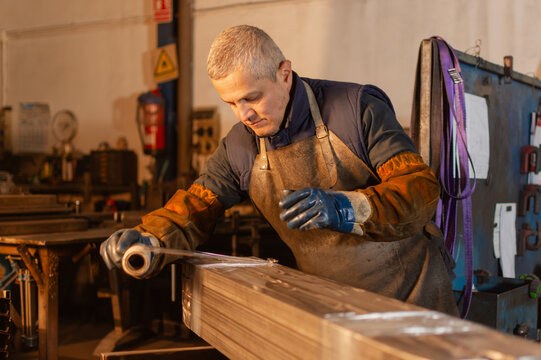 Industrial worker wrapping welded metal pieces in protective plastic