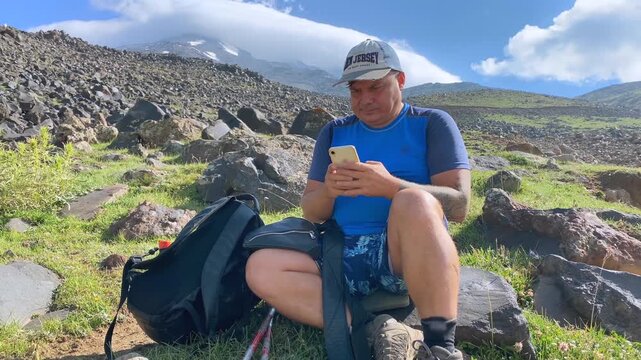 Tourist checking phone front view at a mountain rest stop on Mount Ararat, with backpack and rocky alpine terrain, showing trekking navigation, adventure travel, and outdoor recreation in Turkey