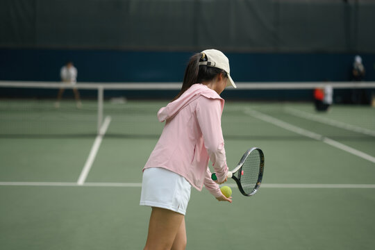Young Asian Woman Playing Tennis on Outdoor Court, Rear View with Racket and Ball