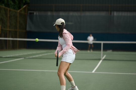 Young Asian Woman Playing Tennis on Outdoor Court, Ready to Hit Ball with Racket