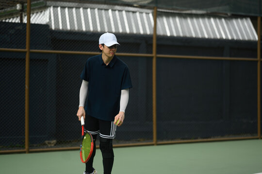 Asian Male Tennis Player Holding Racket and Ball on Outdoor Court Ready to Serve