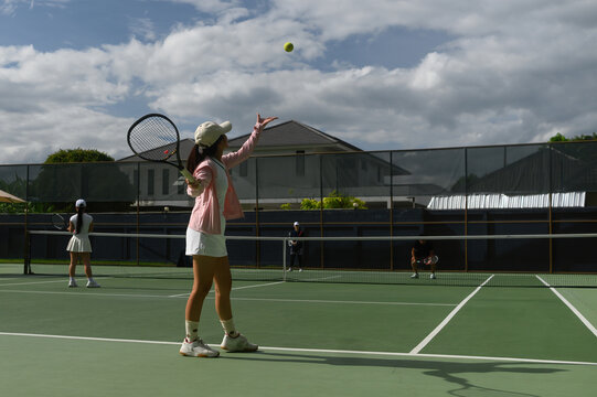 Young Woman Serving in Outdoor Tennis Doubles Match on Green Hard Court