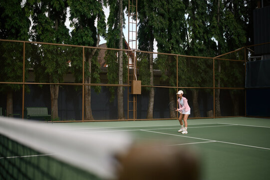 Young Asian Woman Playing Tennis on Outdoor Green Court Surrounded by Trees