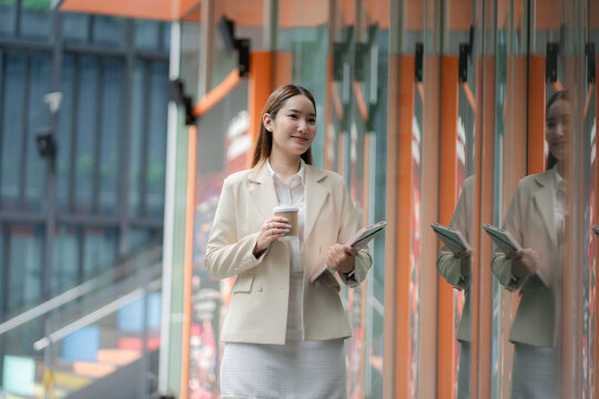 Happy workday concept. Smiling businesswoman walks with coffee and tablet in a modern office district. businesswoman, workday, coffee, professional, career, corporate lifestyle