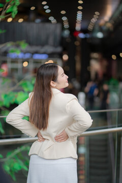 Office syndrome concept showing a businesswoman holding her painful lower back after work, suggesting muscle strain and discomfort. lower back pain, office syndrome, strain, fatigue, posture