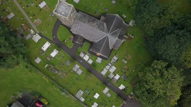 Top down aerial over the roof of St Michael's Church of Ireland and the rows of headstones in its graveyard, County Tyrone, Northern Ireland