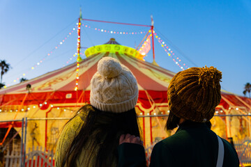 Two young women enjoying a fun night at the circus, watching the illuminated big top tent at a carnival festival © Alberto