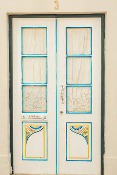 A colorful door stands at the front of a historic building. The door has blue and white frames and decorative patterns. Sunlight brings out the bright colors of the yellow walls.