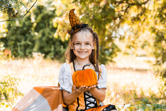 Girl in Halloween Costume Holds a Pumpkin While Sitting Outdoors During Autumn in October With Spiderwebs in the Background