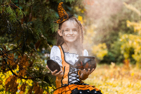 Girl Dressed for Halloween Holds Bowls in a Garden Surrounded by Autumn Leaves and Decorations While Celebrating the October Season