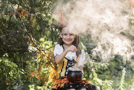 Girl Enjoys Halloween in the Garden Surrounded by Autumn Colors and Decorations Including a Pumpkin and Spiderwebs While She Plays With a Cauldron