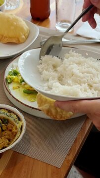 Person serving steamed rice with traditional curry and crisp papadum bread at restaurant table