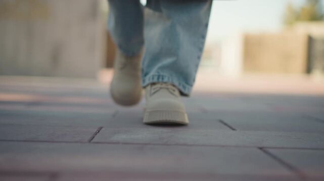 Close up of person feet in white shoes and blue jeans walking steadily on pavement. focus remains consistently low angle capturing rhythmic movement through outdoor environment with soft