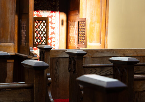 Traditional wooden church pews and carved wooden confessional booth illuminated by warm sunlight, historic church interior with brick wall