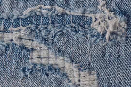 Close up shot distressed blue jeans fabric showing frayed edges and white woven threads.