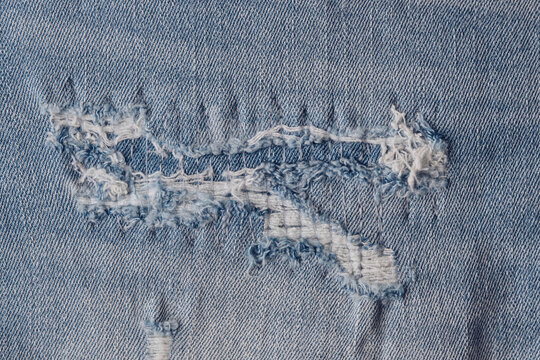 Close up distressed light blue jeans showing torn fabric patches and loose white threads.