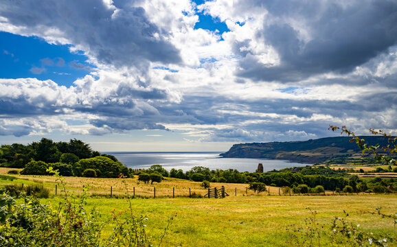 Dramatic clouds and sunlight over fields and the North Sea near Robin Hood&rsquo;s Bay, with the rugged Yorkshire coastline stretching towards Ravenscar, North Yorkshire, England.
