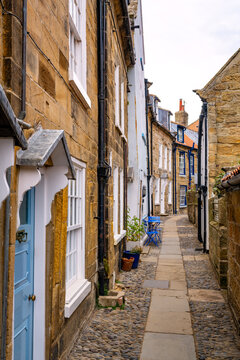 Narrow cobbled lane lined with traditional sandstone cottages, white windows and colourful doors in the historic fishing village of Robin Hood&rsquo;s Bay, England.