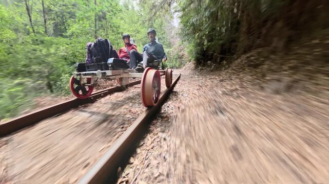 A couple rides an electric railbike over old railroad tracks in a forest of redwoods near Mendocino California.