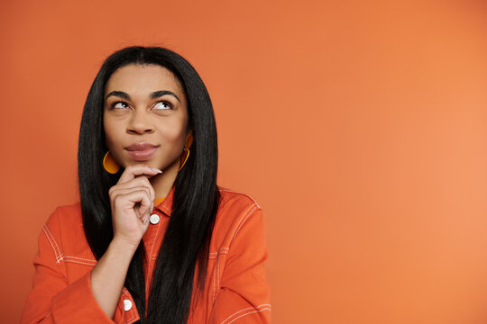 Young woman thoughtfully poses against a vibrant orange background while contemplating something new