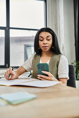 Obraz premium A woman concentrates on her phone while surrounded by papers and natural light.