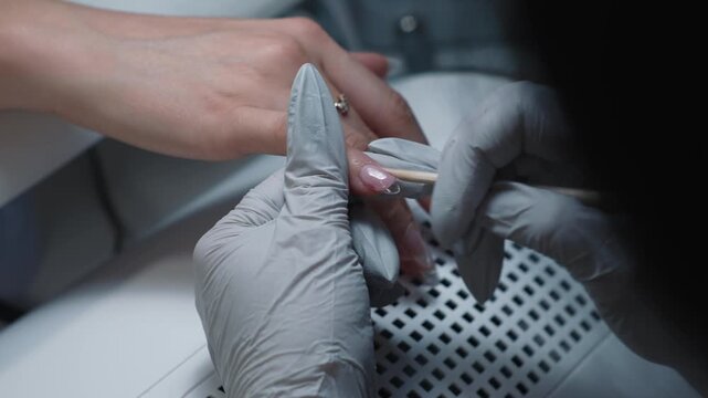 Nail technician evenly applies polygel with orange stick on nail surface during nail extension procedure in beauty salon