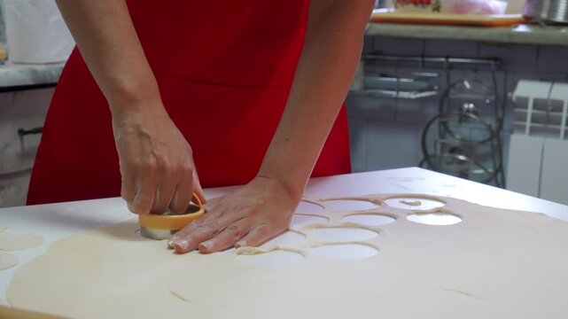 A focused baker carefully cuts circles from rolled dough using a round cutter. She works on a clean white kitchen table with patient joy.