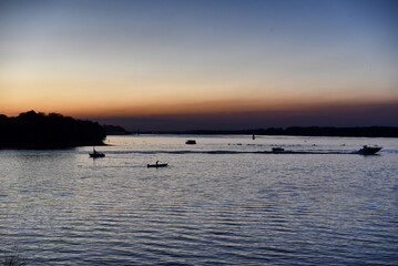 Obraz premium Boats sailing on a wide river during twilight dusk with orange and blue sky horizon