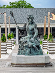 Hyannis, Massachusetts, USA - June 26, 2026: Neptune's statue on which he caresses a turtle, in front of Neptune's gathering spot, a bar where concerts and dance festivals happen © Klodien