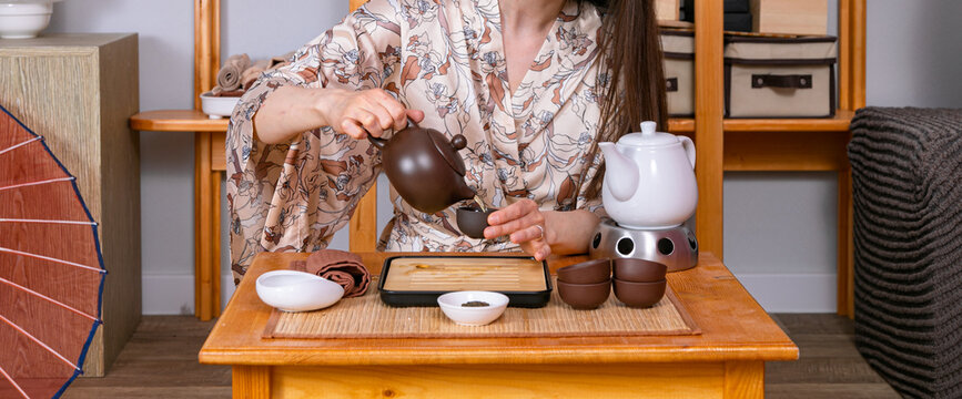 Woman pouring tea from ceramic pot into small cup during tea ceremony. Traditional Asian hot beverage preparation process. Ritual of relaxation, mindfulness and zen culture practice