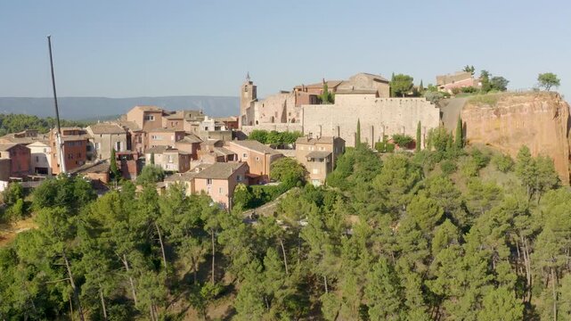 Aerial slow pan revealing ochre stone houses and red tile roofs in Roussillon village, Provence, high angle shot
