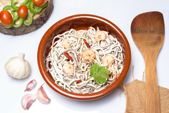 Traditional Spanish dish of gulas surimi baby eels cooked with garlic and prawns served in a classic brown clay ramekin on a white background