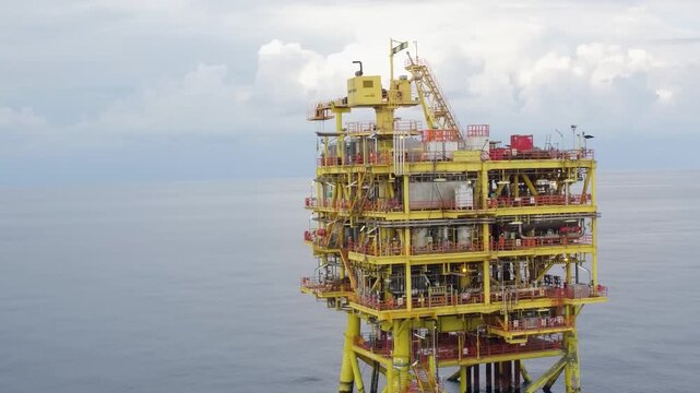 Offshore oil rig showing visible action, in open ocean, with oil rig, cloudy sky, from a aerial perspective, with yellow, red accents, and industrial mood, with nearby objects.