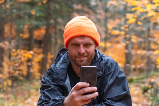 hiker in the forest trail, looking at his phone, hunting sesason hat, what wether outdoor activities with smart phone