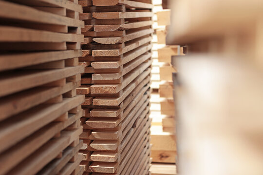 Close-up view of stacked wooden planks. Visible wood grain texture. Depth perspective with blurred background. Industrial lumber storage