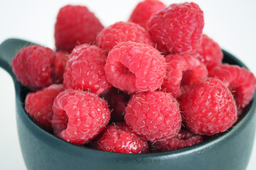 Raspberries in a black cup against a light background. Close-up of juicy, ripe berries. Food. Sweet berries harvested by farmers during the summer season. Organic. Vitamins. healthy raspberries. © Tatuss