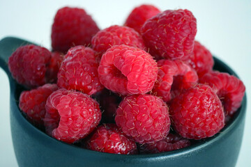 Raspberries in a black cup against a light background. Close-up of juicy, ripe berries. Food. Sweet berries harvested by farmers during the summer season. Organic. Vitamins. healthy raspberries. © Tatuss