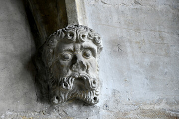 A close-up view of a carved stone wall corbel shaped as a bearded male face with stylized curly hair and mustache, supporting an arch inside Prague Castle. © IbrahimAlkan