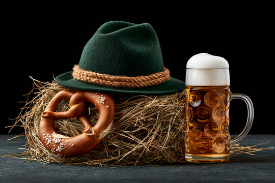 Tyrolean hat feather pretzel and beer mug on wooden table, moody Oktoberfest still life