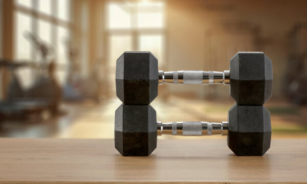 Dumbbells on wooden bench with blurred gym interior &ndash; fitness and strength training concept