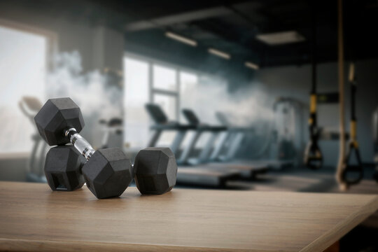 Dumbbells on wooden bench with blurred gym interior &ndash; fitness and strength training concept