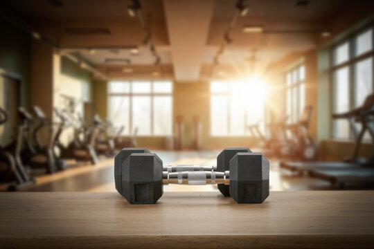 Dumbbells on wooden bench with blurred gym interior &ndash; fitness and strength training concept