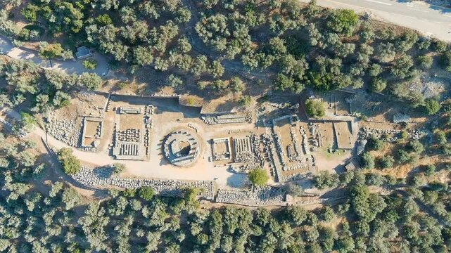 Delphi, Greece. The circular Tholos of Athena Pronaia, its reconstructed Doric columns rising from ancient stone foundations, Drone footage over the Sanctuary of Athena under bright summer morning li