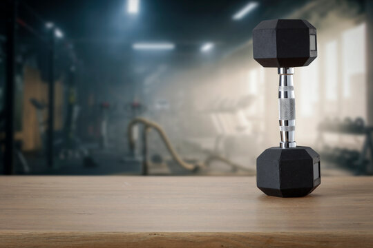 Dumbbells on wooden bench with blurred gym interior &ndash; fitness and strength training concept