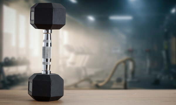 Dumbbells on wooden bench with blurred gym interior &ndash; fitness and strength training concept