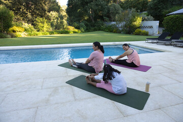 Diverse female family stretching on yoga mats beside pool on tiled patio with water bottle © WavebreakMediaMicro