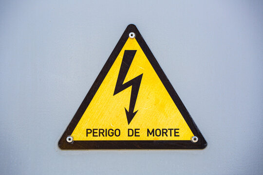 Perigo de Morte warning sign with a lightning bolt symbol, cautioning danger of death from electricity, mounted on a metal panel for safety awareness.