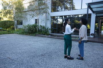 Diverse female colleagues conversing outside glass entrance on forecourt with wristwatch © WavebreakMediaMicro