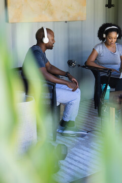 Diverse co-hosts recording in studio in casual clothes wearing headphones with boom mic and laptop
