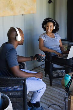 Diverse co-hosts wearing white headphones recording in container room with laptop boom mic